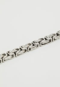 Catena in metallo argento con anelli rettangolari interconnessi. Finitura lucida e texture liscia, che mette in risalto un design moderno e geometrico.