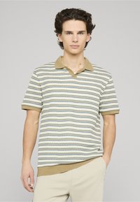 Polo à manches courtes couleur crème avec des rayures horizontales vertes et bleues, doté d'un col à revers et d'un ourlet côtelé. Tissu en mélange de coton.