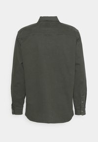 Tummanvihreä pitkähihainen paita, joka on valmistettu pehmeästä kankaasta. Siinä on napitettava kaulus, napilliset kalvosimet ja suora helma selkäkaarrokeyksityiskohdalla.