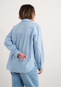 Zila un baltā svītru krekls ar garām piedurknēm, pogājamām aprocēm un izliekto apakšmalu. Izgatavots no viegla auduma, ar aizmugurējo yoku un krokām.