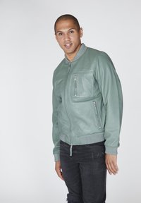 Zelená kožená bomber bunda s ribbeným šedým límcem, dvěma zipovými předními kapsami a ribbenými manžetami, spárovaná s černými popraskanými džíny daří.