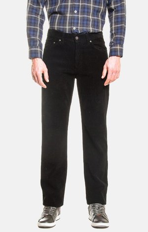 Uomo che indossa pantaloni di velluto a coste neri, camicia a quadri blu e bianca e sneakers nere con suola bianca, in piedi su sfondo bianco.