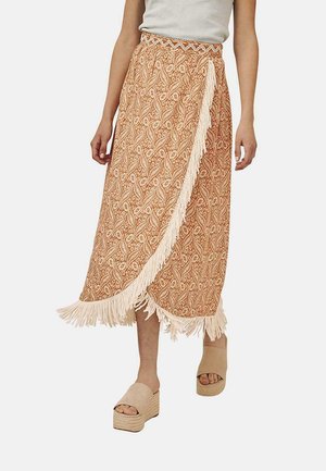 Falda de estampado naranja con flecos, hecha de una tela suave. Presenta una cintura alta y un diseño floral, combinada con sandalias de plataforma beige.