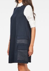 Marinblå shiftklänning med rund halsringning, ärmlös design, två stora framfickor och kontrasterande detaljer i denim. 