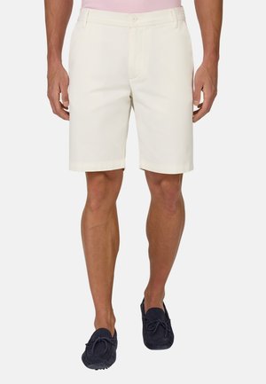 Shorts en coton beige à coupe droite, dotés d'un devant plat, de passants de ceinture et de poches latérales ; associés à des mocassins en daim bleu foncé.