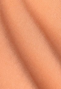 Un textile de couleur pêche avec une texture lisse et douce, présentant de subtils lignes diagonales et une qualité fine et légère.