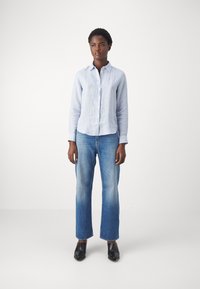 Jasnoniebieska lniana koszula z guzikami, w połączeniu z jasnoniebieskimi spodniami typu straight-leg i czarnymi czółenkami na obcasie. Prosty i nowoczesny styl.