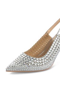 Décolleté argentato con tacco alto e punta affusolata, decorato con strass trasparenti circolari e un dettaglio a scallop lungo il bordo.