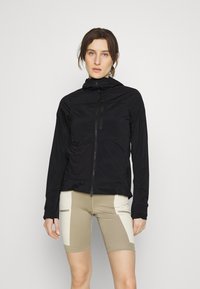 Sort letvægtsjakke med lynlås foran og hætte. Kombineret med beige shorts med crema paneler og to små lynlås-lommer.