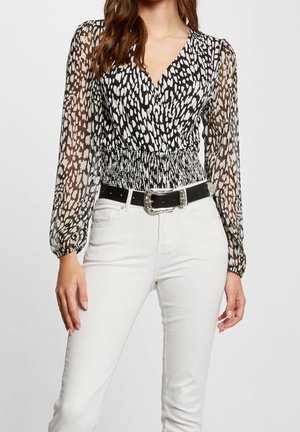 Schwarz-weiß gemusterte Bluse mit transparenten langen Ärmeln, gerafftem Bund und V-Ausschnitt, kombiniert mit weißen Hosen und einem schwarzen Gürtel.