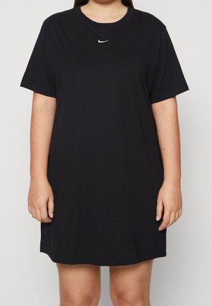 Osoba nosząca czarną sukienkę typu T-shirt Nike z krótkim rękawem z białym logo Nike swoosh na piersi, widoczną od szyi do ponad kolan.