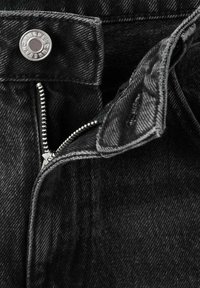 Le tissu en denim noir présente un gros plan d'une fermeture éclair avec un curseur en argent et une fermeture à bouton, mettant en valeur des détails subtils de texture et de couture.