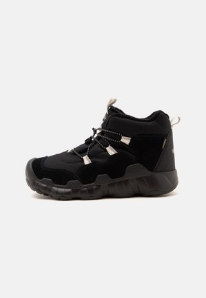 Chaussure de randonnée noire mi-haute avec semelle texturée, passants réfléchissants pour lacets, col rembourré et languettes de traction sur fond blanc.