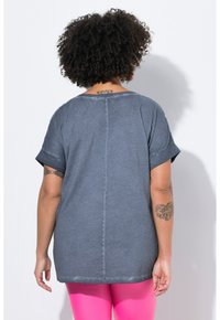 Grå, løstsiddende T-shirt med opkrøllede ærmer, blød tekstur og detaljeret midtersøm. Bæres med lyserøde leggings.