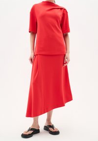 Rode tweedelige outfit met een top met korte mouwen en een asymmetrische rok. Gemaakt van een gladde stof; heeft een relaxte pasvorm en minimale naden.