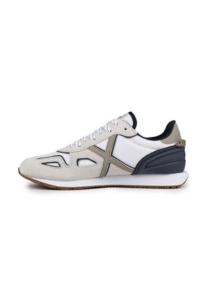 Zapatilla con combinación de textil blanco y gamuza beige, con un talón de acento negro, puntera redondeada y detalles de costura en contraste.