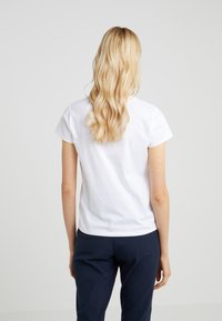 Vit bomull t-shirt med rund halsringning och korta ärmar, kombinerad med marinblå byxor. Har en enkel, odekorerad design.