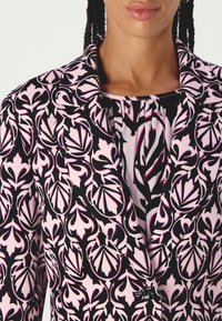 Patterned blazer featuring a black, pink, and white floral design, with a sharp collar and a single button closure. Smooth fabric texture.