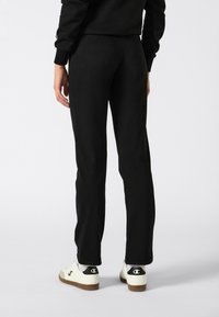 Black sweatpants with a slim fit, featuring a smooth texture. Paired with white sneakers that have a black logo on the heel.