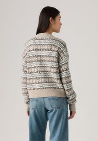 Gebreide trui in cremewit, beige en bruin met een geometrisch patroon. Beschikt over geribbelde manchetten en onderrand, heeft een losse pasvorm en een ronde halslijn.