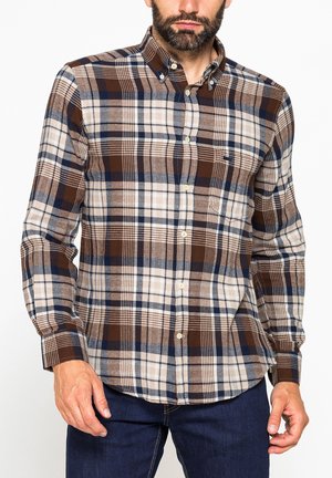 Uomo che indossa una camicia a quadri marrone, blu navy e beige con taschino e jeans blu scuro, su sfondo bianco.