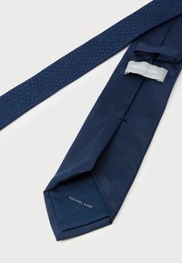 Marineblaues Krawatte mit glatter Textur und dezentem Mustergewebe. Etikett "MICHAEL KORS" auf der Unterseite eingenäht.