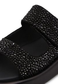 Sandal nera con tomaia texturizzata e decorazioni nere, due cinturini e suola spessa, che offre una vestibilità sicura e un design elegante.