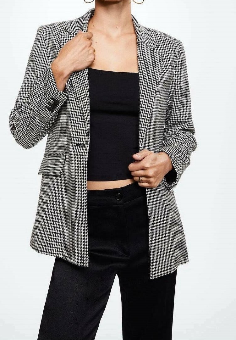 Femme portant un top bandeau noir, un pantalon noir et un blazer pied-de-poule noir et blanc, ajustant le revers du blazer d'une main.