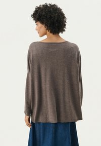 Bruine, oversized trui met een ruime halslijn en een drop shoulder-design. Zacht materiaal met een gladde textuur, in combinatie met een spijkerrok.