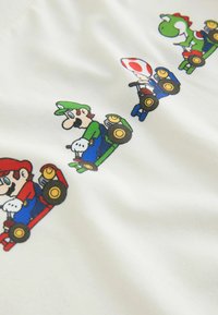 Weißer Stoff mit bunten Cartoonfiguren in Go-Karts: Mario (rot), Luigi (grün), Toad (blau) und Yoshi (grün mit roten Akzenten).