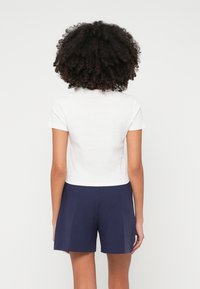 Balta sarausta t-krekls mīkstā audumā, kombinēts ar tumši ziliem šortiem. T-kreklam ir īsas piedurknes un apaļa kakla izgriezums.