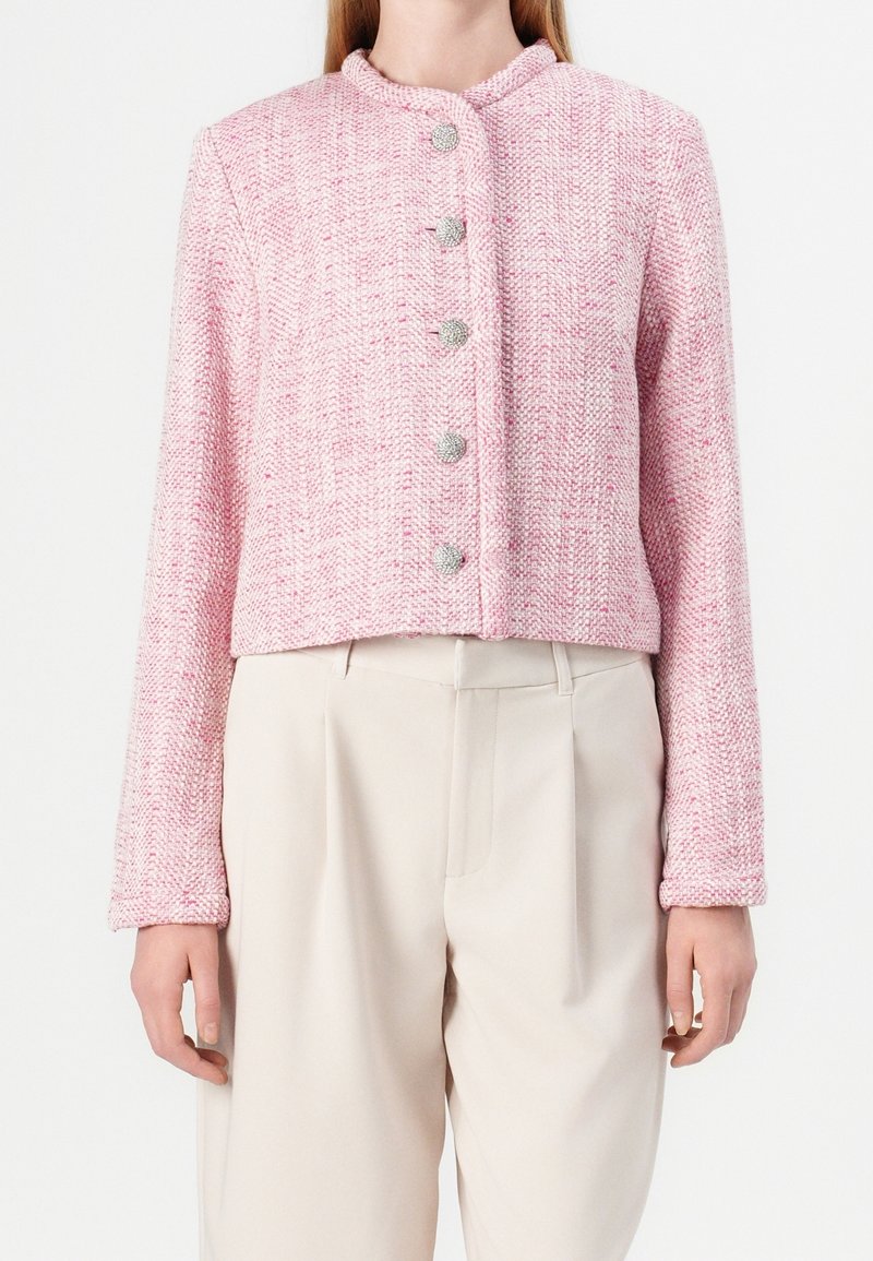 Růžový tweedový krátký kabátek s kulatým límcem, s pěti stříbrnými knoflíky vpředu a texturovanou tkaninou ve vzoru rybí kosti.