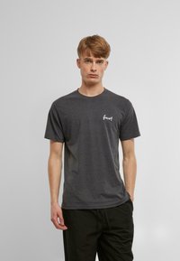 Graues Baumwoll-T-Shirt mit kurzen Ärmeln, Rundhalsausschnitt und weißem "forever" Textlogo auf der linken Brustseite, kombiniert mit dunklen Hosen.