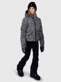 Giovane donna che indossa una giacca invernale con stampa leopardata, guanti abbinati, pantaloni neri, stivali neri e un cappellino nero, in piedi contro uno sfondo grigio.
