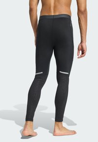 Čierne športové legíny s priliehavým strihom, s reflexnými akcentmi na lýtkach a textúrovanými vzormi pozdĺž dolných nôh.