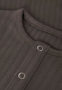 Geribbelde bruine brei stof met een ronde halslijn. Heeft zilveren knoopsluitingen en textuurpatronen over het materiaal.