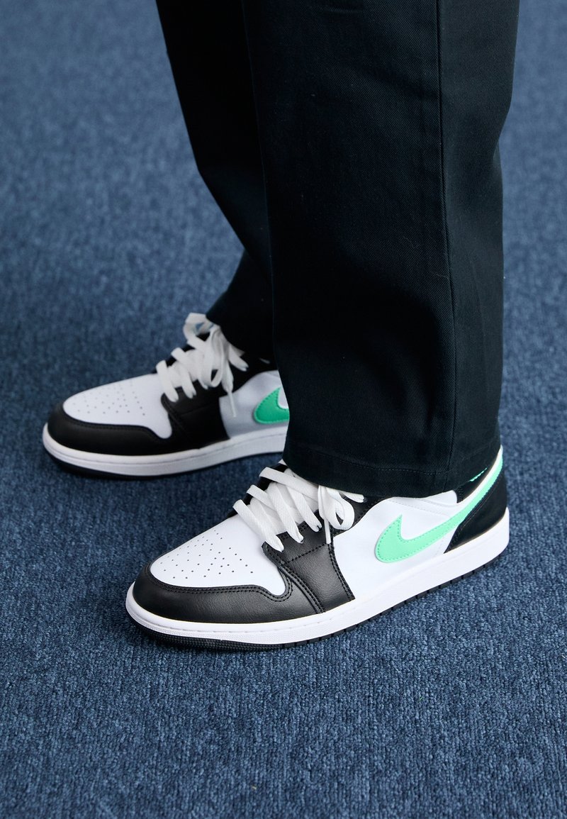 Czarno-białe niskie sneakersy z miętowym logo Nike. Posiadają perforowaną część noska oraz białe sznurówki. Noszone z czarnymi spodniami.