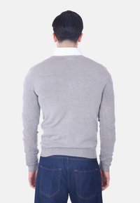 Maglione grigio chiaro con colletto rotondo, polsini e orlo a coste, realizzato in un morbido materiale a maglia, indossato sopra jeans in denim scuri.