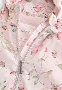 Veste de pluie légère rose avec un motif floral, une fermeture éclair à l'avant et une capuche. L'étiquette intérieure indique "NEXT" avec une doublure douce.