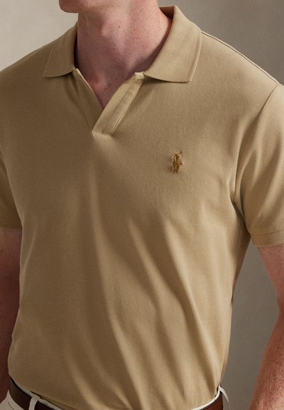 Μπεζ πόλο μπλούζα με υφή πλέξης, διαθέτει κλασικό γιακά και κοντά μανίκια. Μικρό κεντημένο λογότυπο στο αριστερό στήθος.