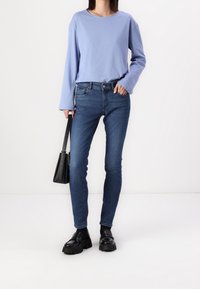 Světle modrý dlouhý rukáv top spárovaný s tmavě modrými skinny džíny. Černá kabelka s krátkým držadlem a silné černé loafers.