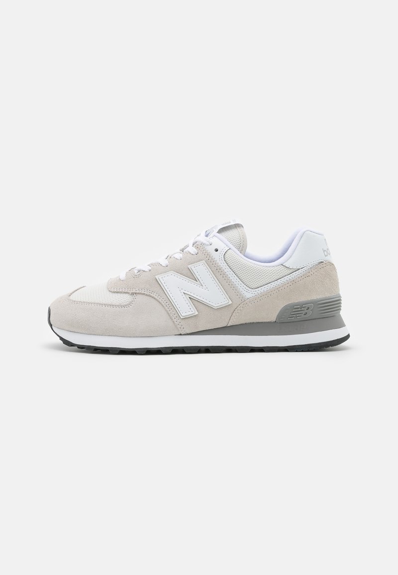 Zapatillas de color beige claro que combinan materiales de ante y malla. El diseño incluye un logotipo blanco prominente y acentos grises. Suela de goma.