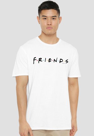 Man with short black hair wears white t-shirt with colorful "FRIENDS" text in bold letters on chest, standing against plain background.
