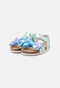 Metalliska mintgröna sandaler med justerbara remmar och stora iriserande blå rosetter framtill. Naturligt kork fotbädd med vit sula.