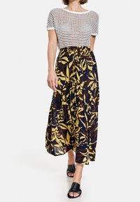 Un haut à manches courtes blanc rayé associé à une jupe maxi florale bleu foncé ornée de feuilles jaunes, brunes et vertes. Des sandales noires à enfiler.