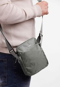 Šedá crossbody taška vyrobená z texturované látky, s hlavním zipovým uzávěrem, nastavitelným popruhem a přední kapsou s jemným vzorem.