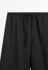 Black elastic waistband pants with tied drawstring, shown from waist to mid-thigh on white background.