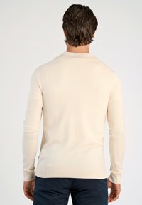 Ljusbeige tröja med långa ärmar, ribbade muddar och nederkant, tillverkad av ett glatt material. Har en klassisk krage och inga synliga mönster.