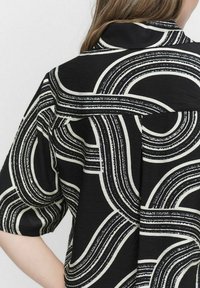 Svart kortärmad skjorta med ett djärvt vitt abstrakt vågmönster. Texturerad tyg med en notch-krage och avslappnad passform.