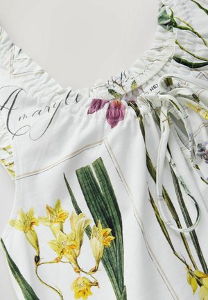 Virágos blúz fehér alapon, sárga és lila virágmintákkal, ráncolt nyakkivágással és állítható húzózsinór részlettel.